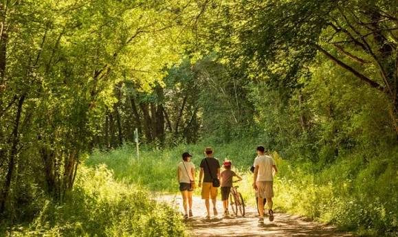 Une famille marche sur un chemin ombragé, un enfant pousse son vélo